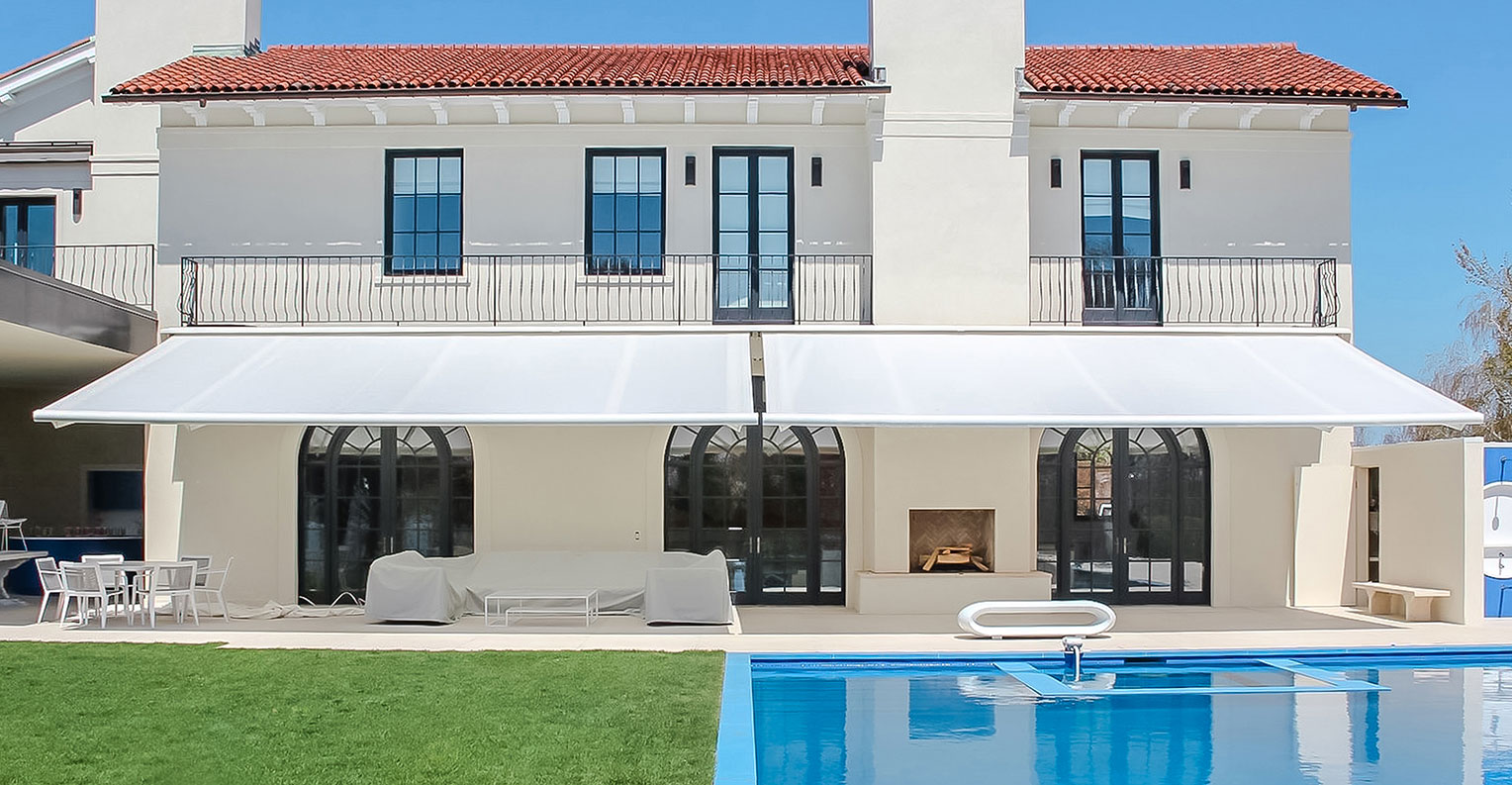 Zwei ausgefahrene weiße Markisen an einem Haus mit Pool