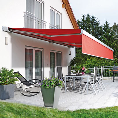 Rote Markise an der Hausfassade über einer Terrasse mit Garten