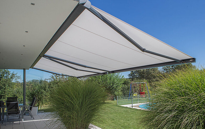 Weiße Markise über einer Terrasse an einem Haus mit Garten