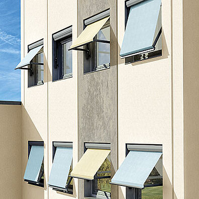 Hausfassade mit mehreren ausgefahrenen Markisen an einem sonnigen Tag