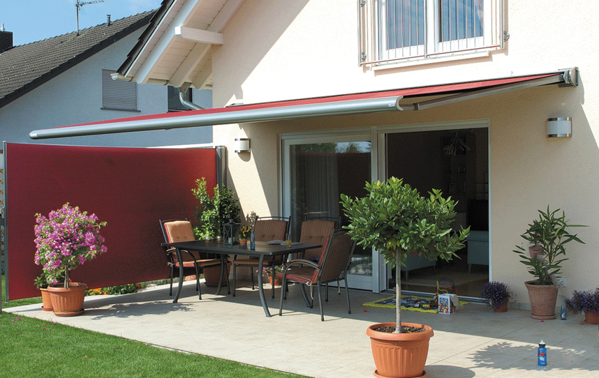 Rote Seitenbeschattung und eine Markise an einer Hausfassade mit Terrasse und Garten