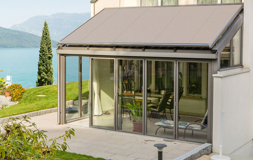 Zwei Glasdachmarkisen auf einer Konstruktion an einer roten Hausfassade mit Garten und Terrasse 