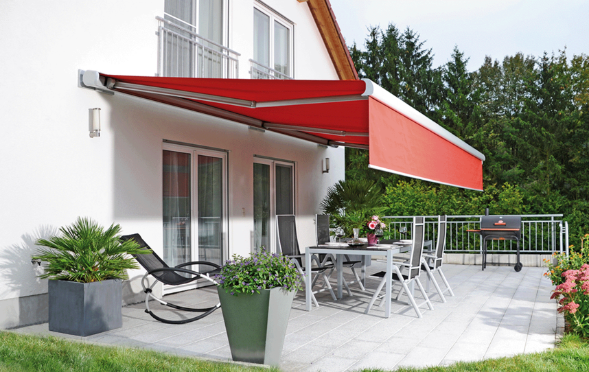 Rote Markise an der Hausfassade über einer Terrasse mit Garten