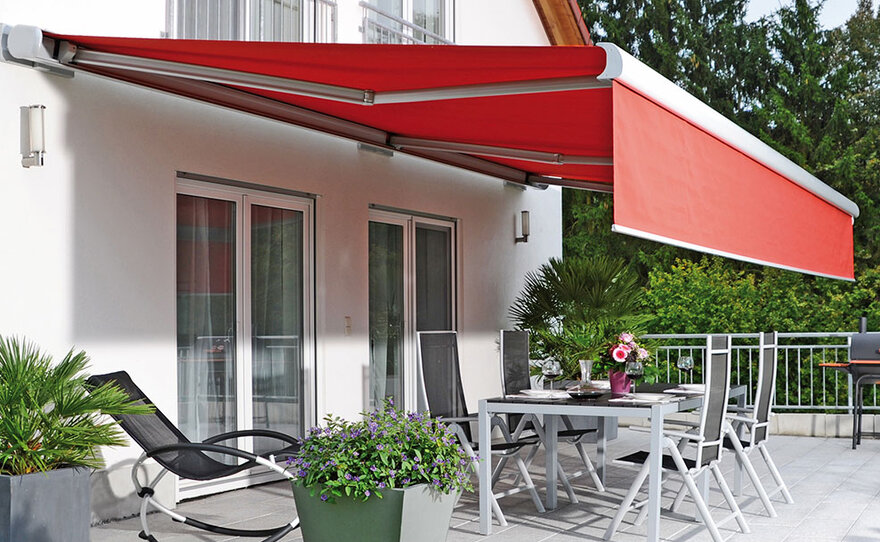 Rote Markise an der Hausfassade über einer Terrasse mit Garten