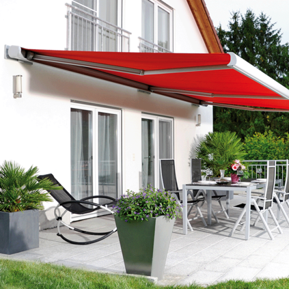 Rote Markise an der Hausfassade über einer Terrasse mit Garten